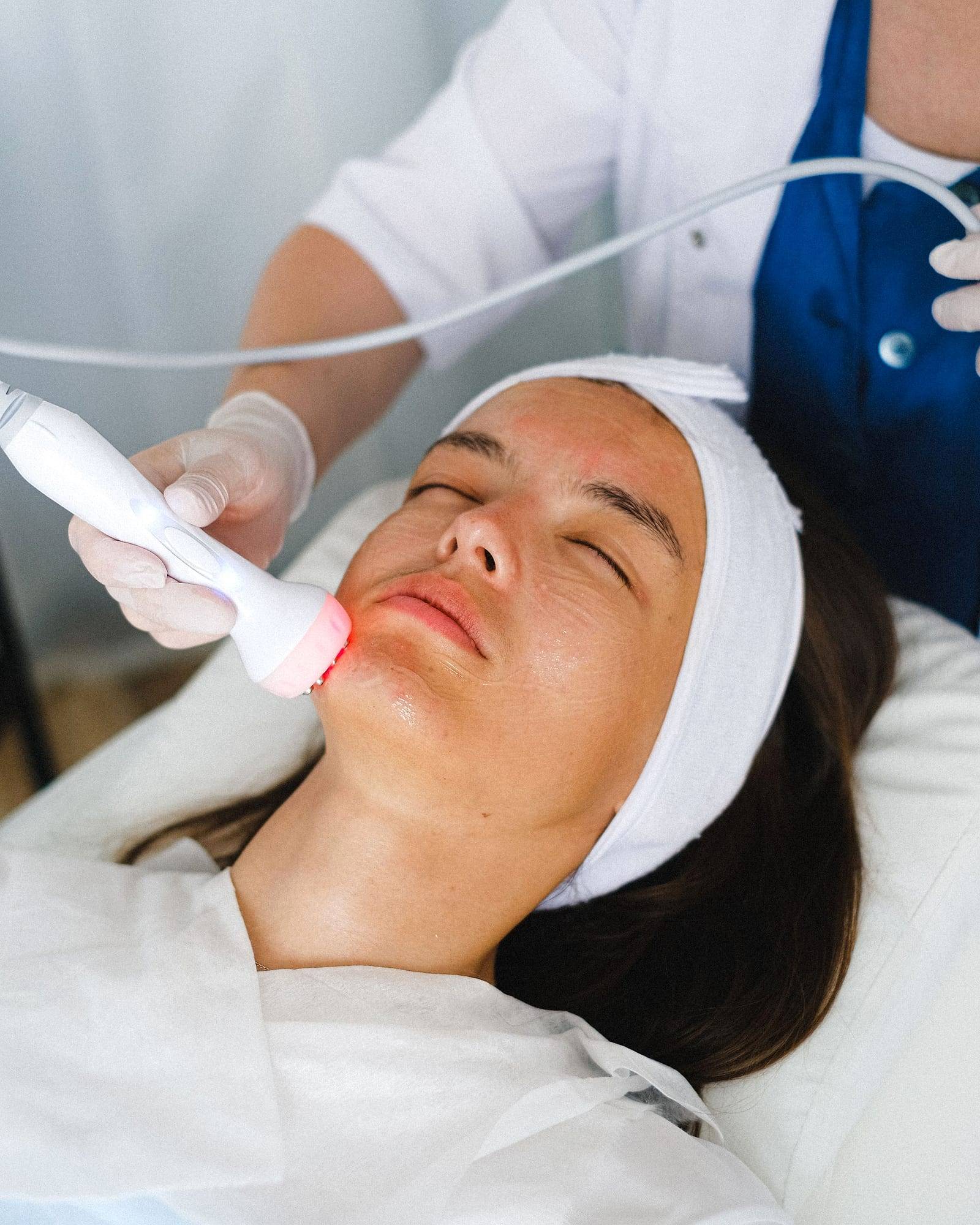Tratamiento facial con aparatología en una clienta relajada con banda en el pelo