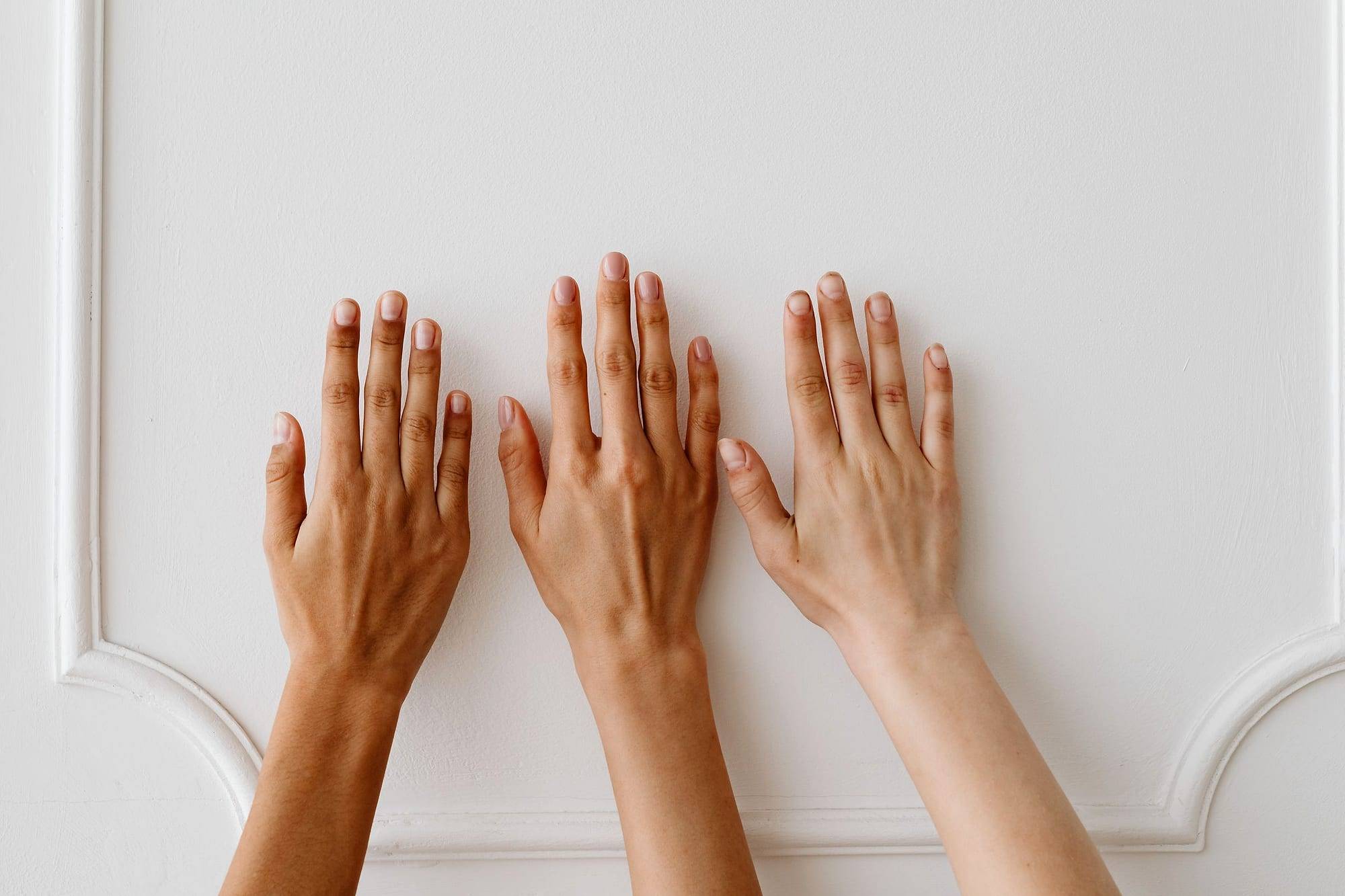 Three hands with different skin tones resting against a white wall