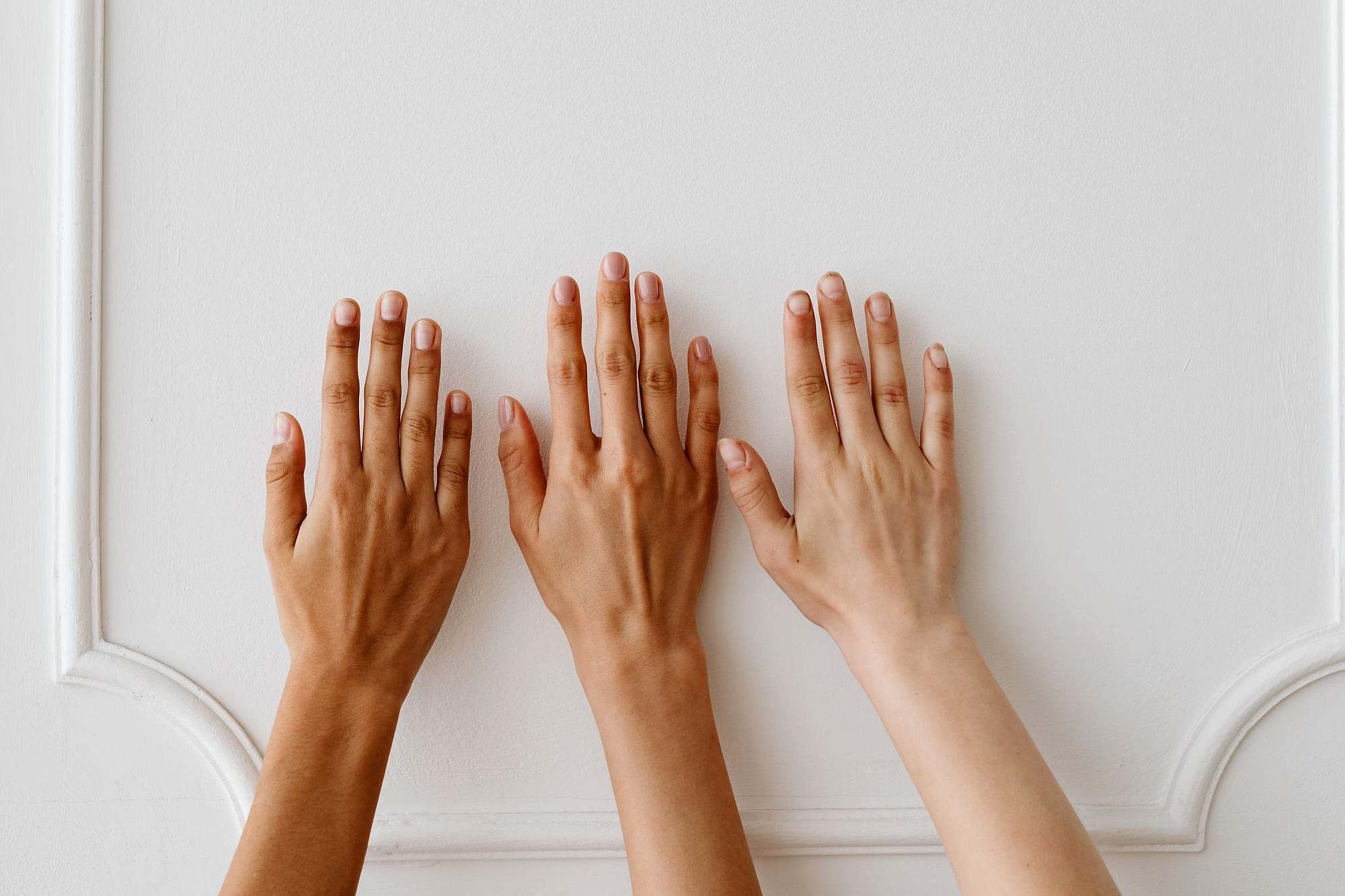 Tres manos con distintos tonos de piel apoyadas sobre una pared blanca
