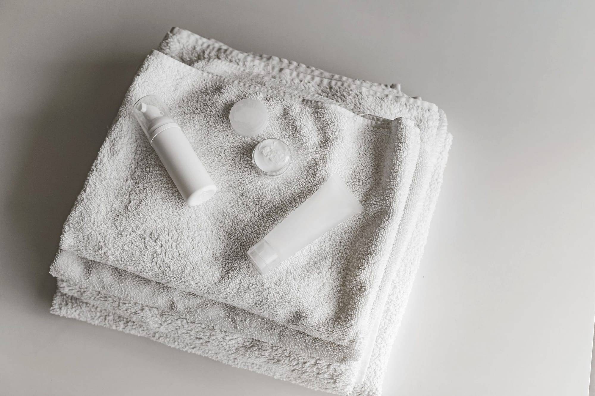 Toallas blancas dobladas con envases cosméticos blancos en una composición minimalista