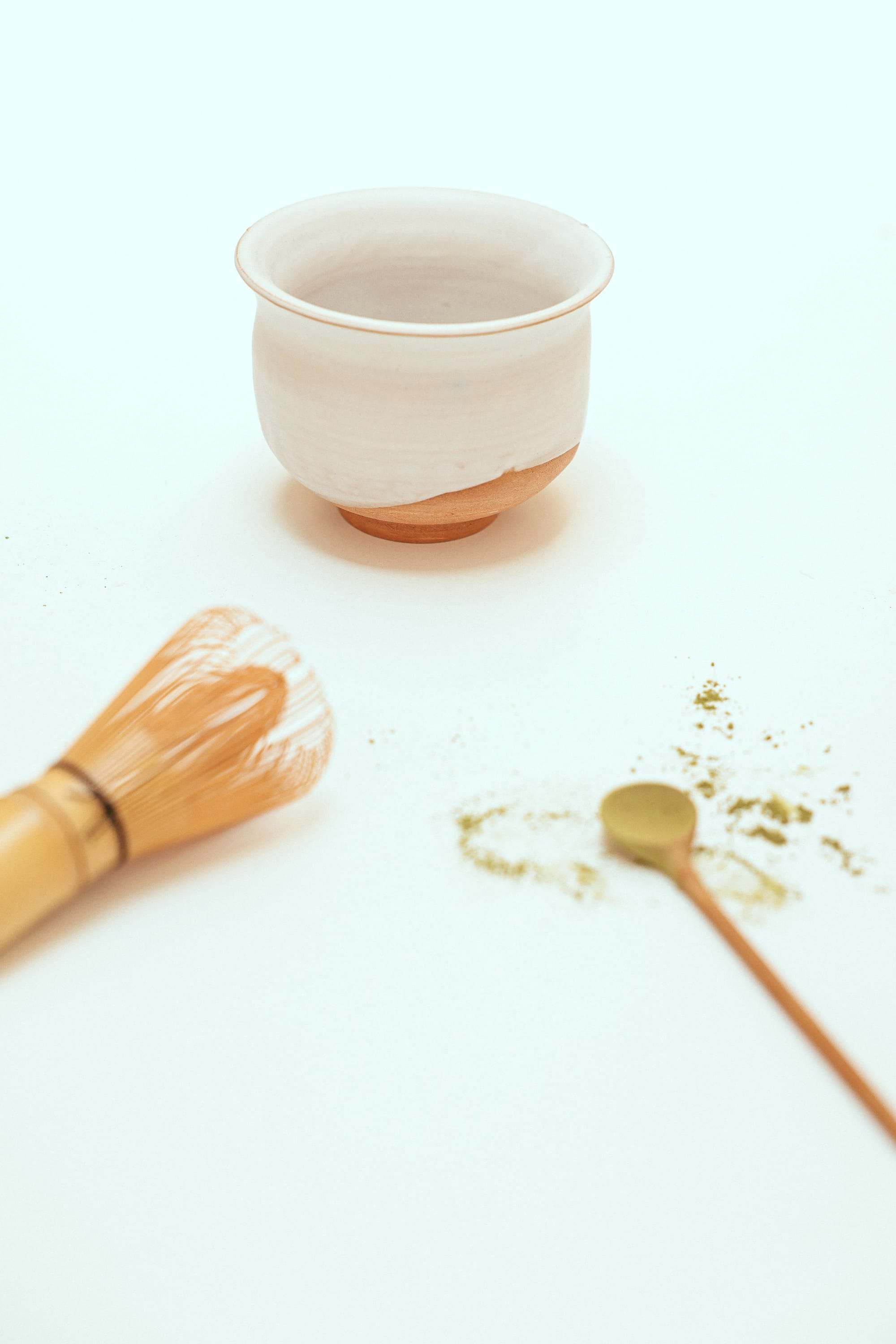 Cuenco de té matcha, batidor de bambú y cucharilla con matcha en polvo sobre fondo blanco