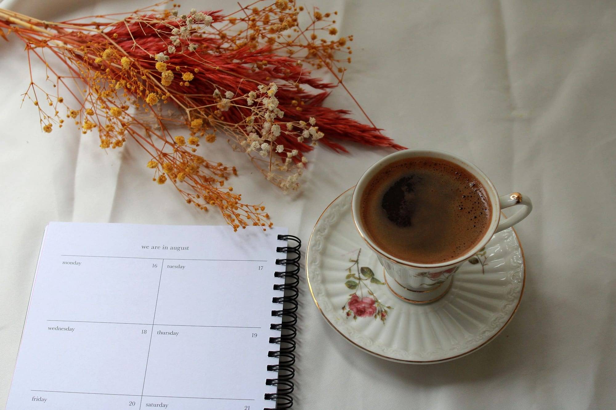 Agenda abierta junto a una taza de café y flores secas sobre un lino claro
