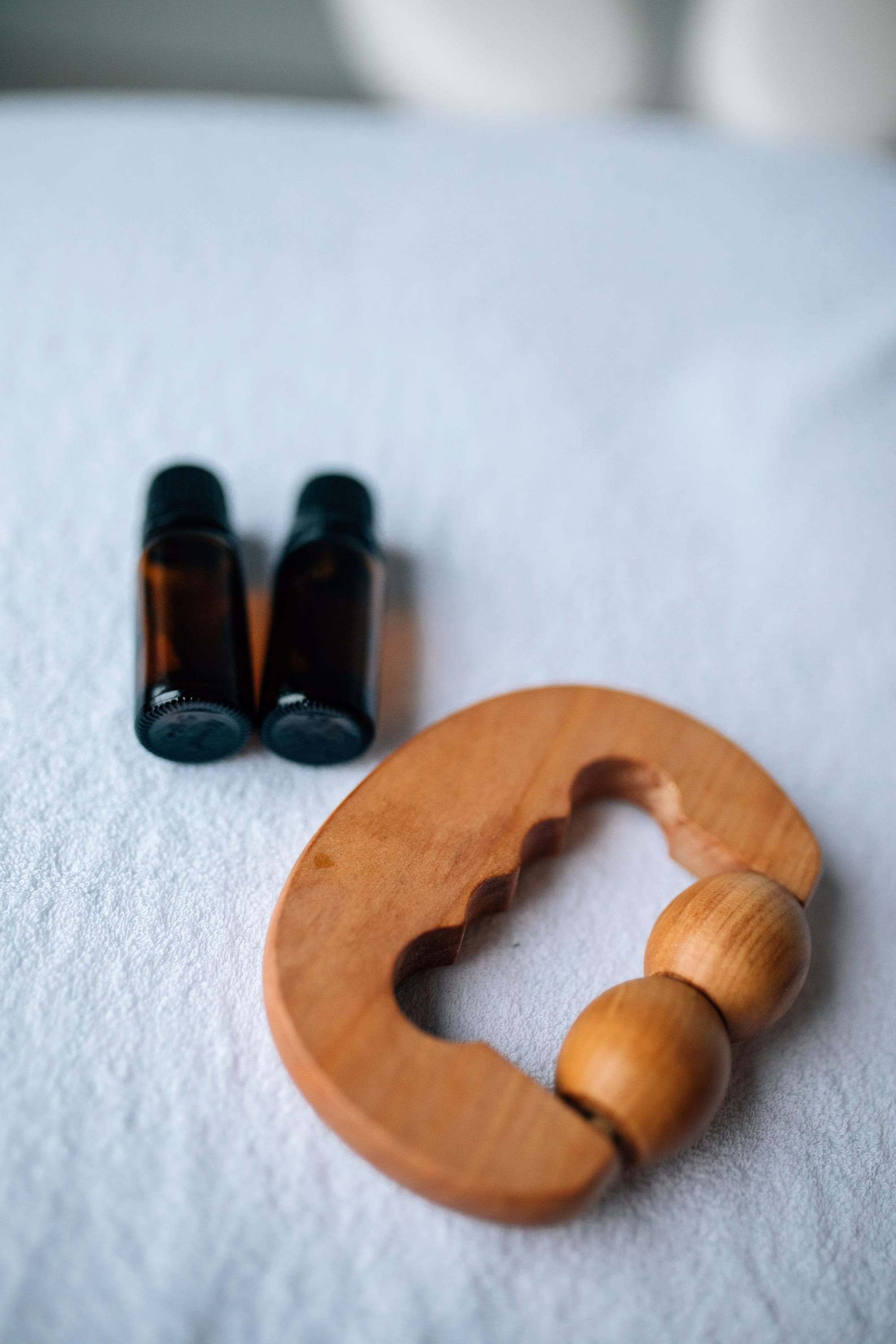 Utensilio de masaje de madera junto a dos frascos de aceite esencial sobre una toalla blanca