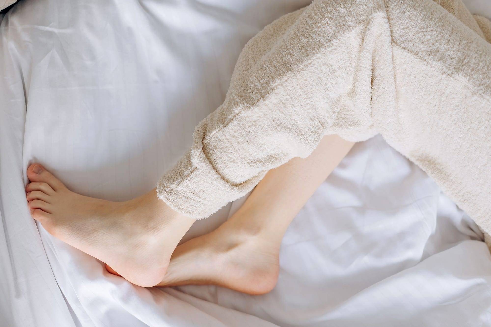 Relaxed legs resting on white bed sheets