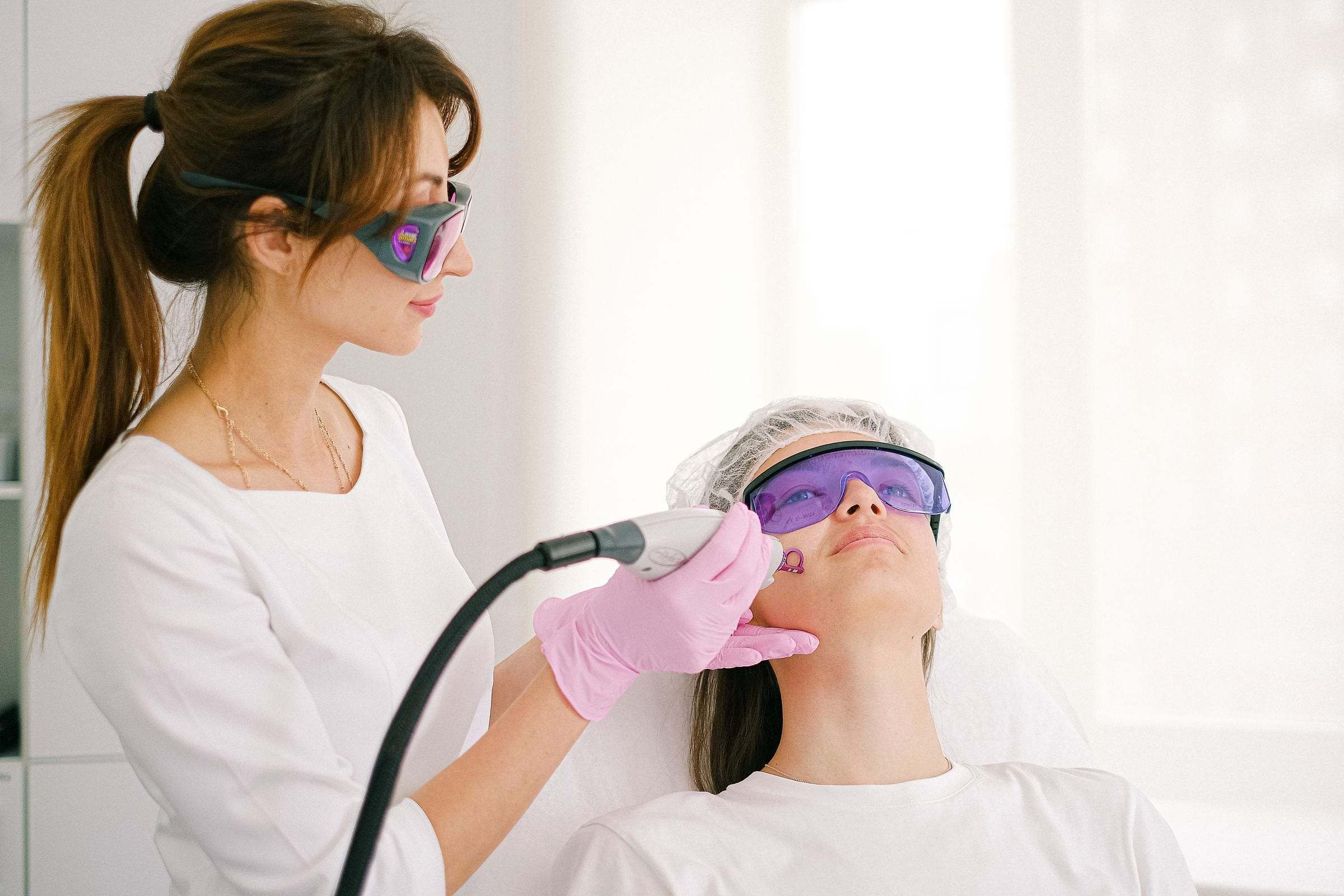 Tratamiento láser facial con gafas protectoras en una cabina luminosa