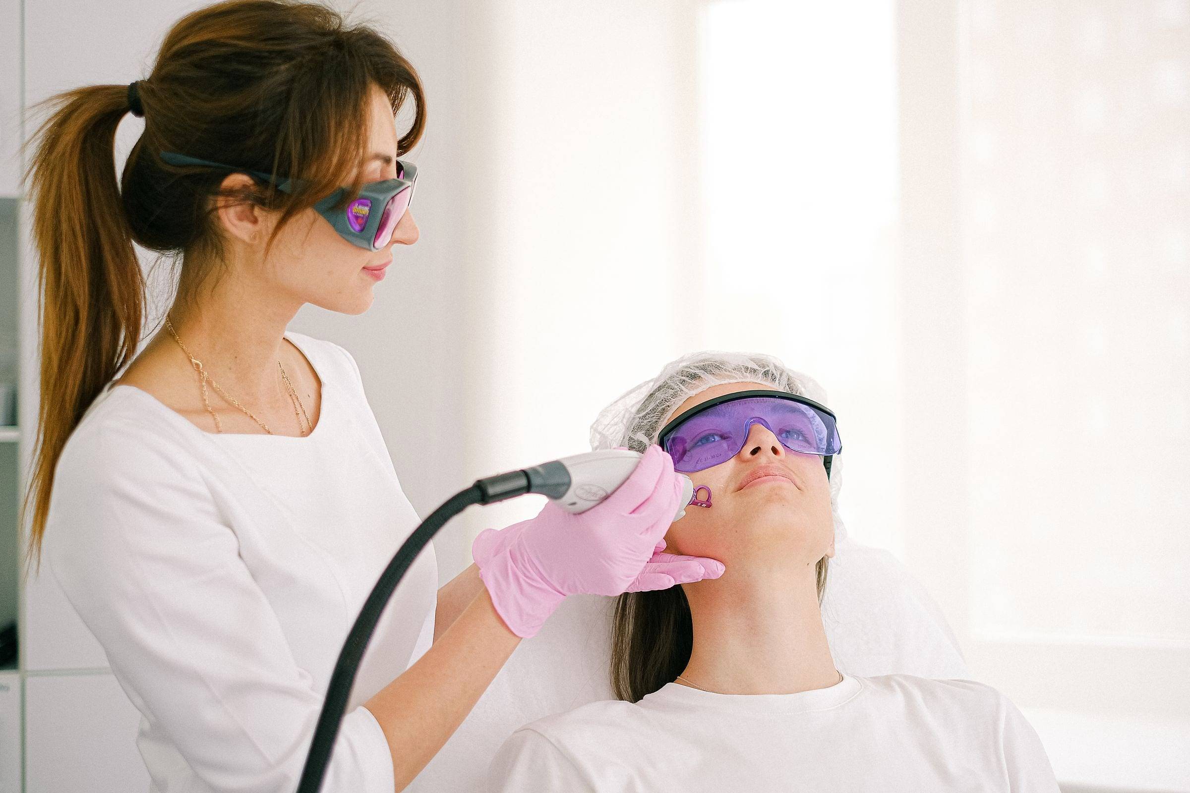Tratamiento láser facial con gafas protectoras en una cabina luminosa
