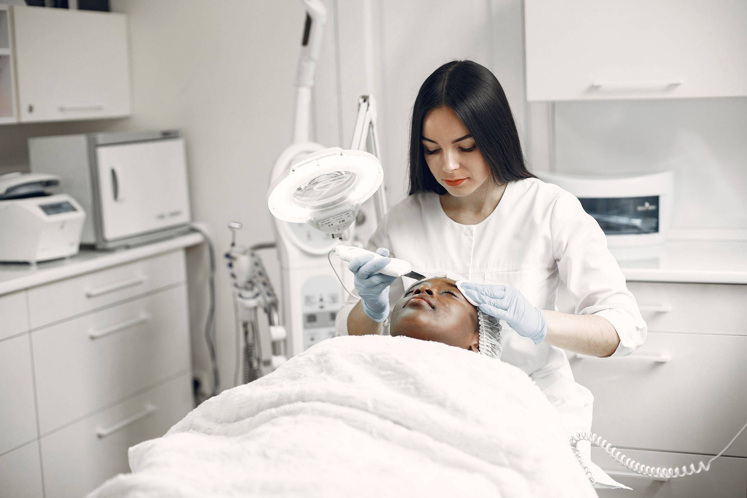 Esteticista realizando una limpieza facial con lupa en una cabina blanca