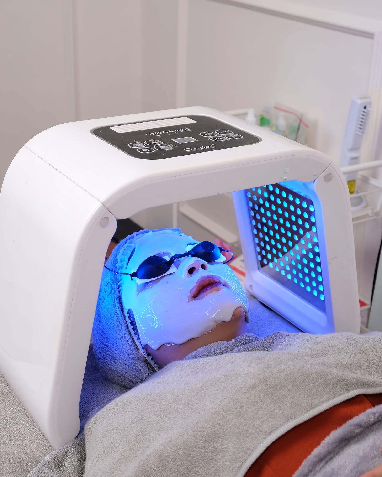Clienta bajo un panel de fototerapia LED azul durante un tratamiento facial