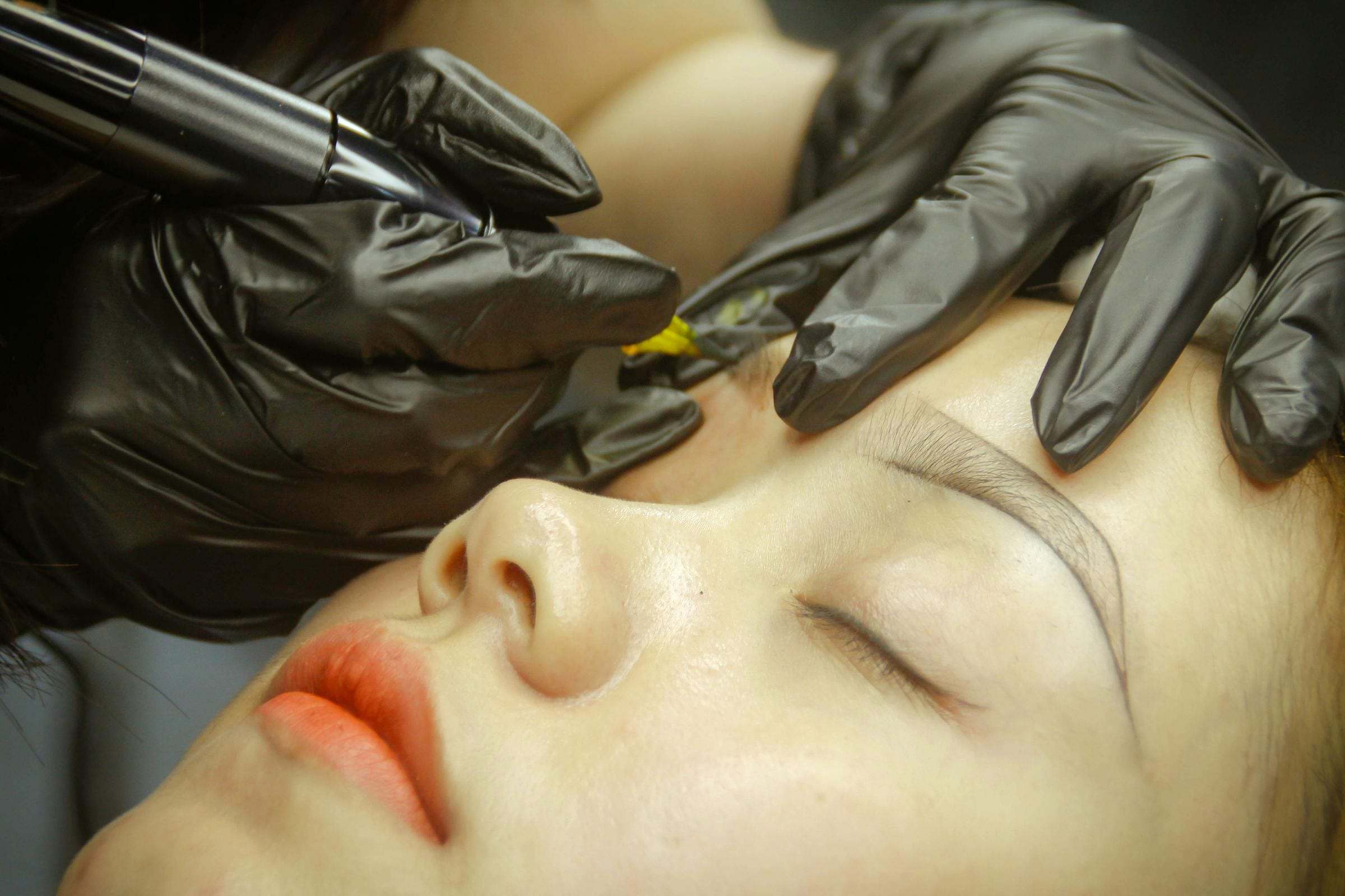 Micropigmentación de cejas: la profesional trabaja la ceja con un dermógrafo y guantes